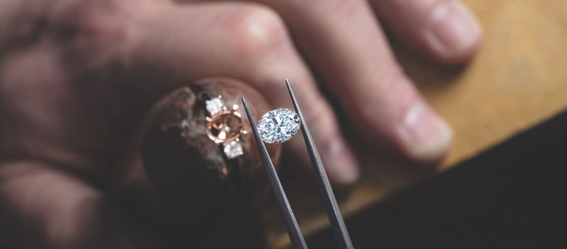Jeweler selecting an oval diamond with tweezers above a custom engagement ring setting at Wedding Bands & Co. in Chicago
