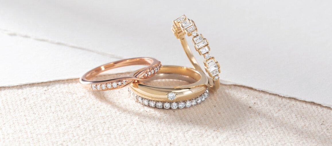 Stacked yellow gold and rose gold wedding bands with round and baguette diamond accents on soft fabric background