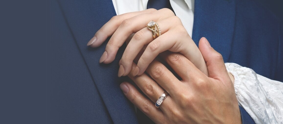Couple holding hands showing yellow gold diamond engagement ring and white gold wedding band symbolizing marriage and commitment