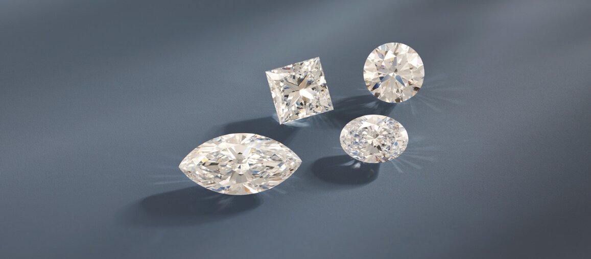 Loose diamonds in marquise, princess, round, and oval cuts displayed on a gray-blue surface to compare diamond shapes