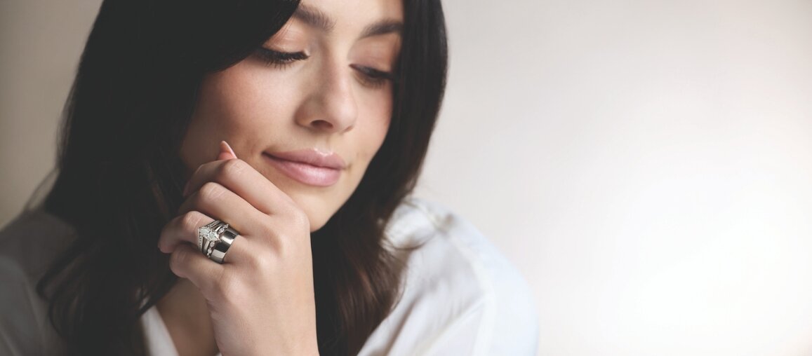 Close-up of woman wearing a diamond wedding band and engagement ring stack on her finger in an elegant lifestyle portrait