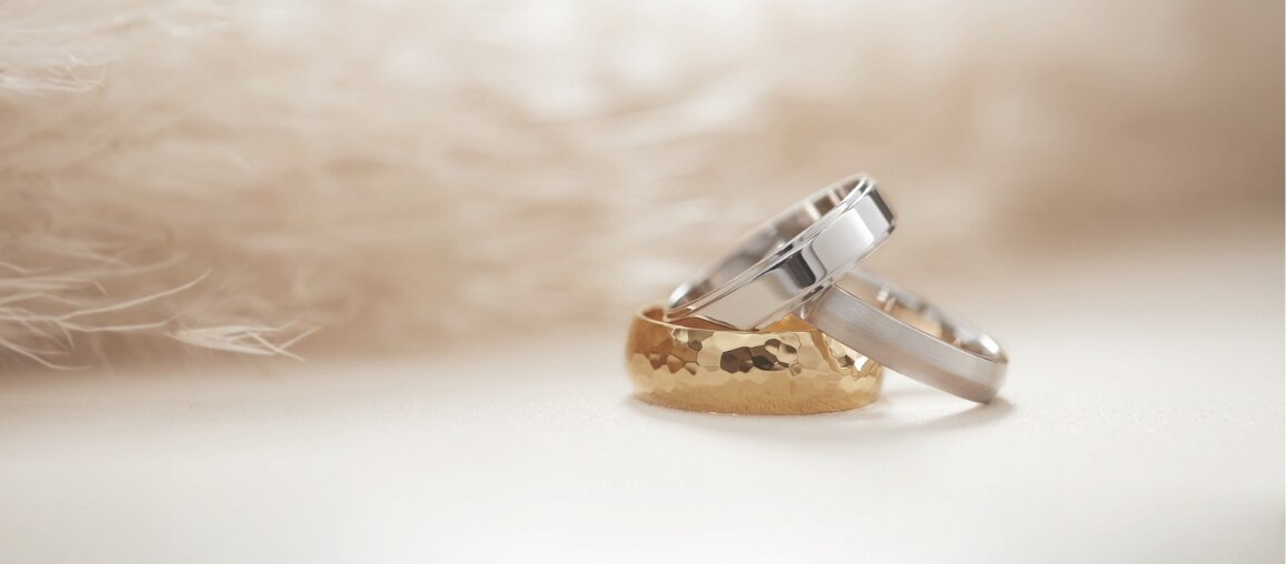 Men’s wedding rings featuring a hammered yellow gold band and a polished white gold band, styled together to showcase modern and classic men’s wedding band designs