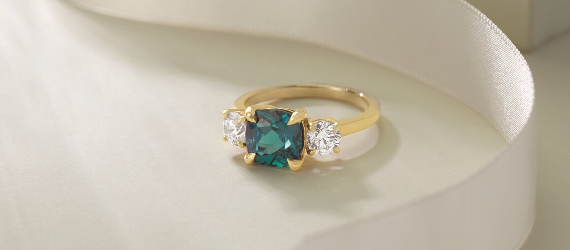 Yellow gold three stone engagement ring featuring a teal center gemstone with round diamond side stones