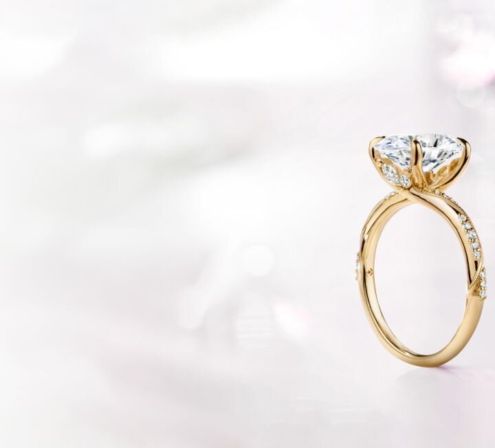 Gold diamond engagement ring against soft white gradient background