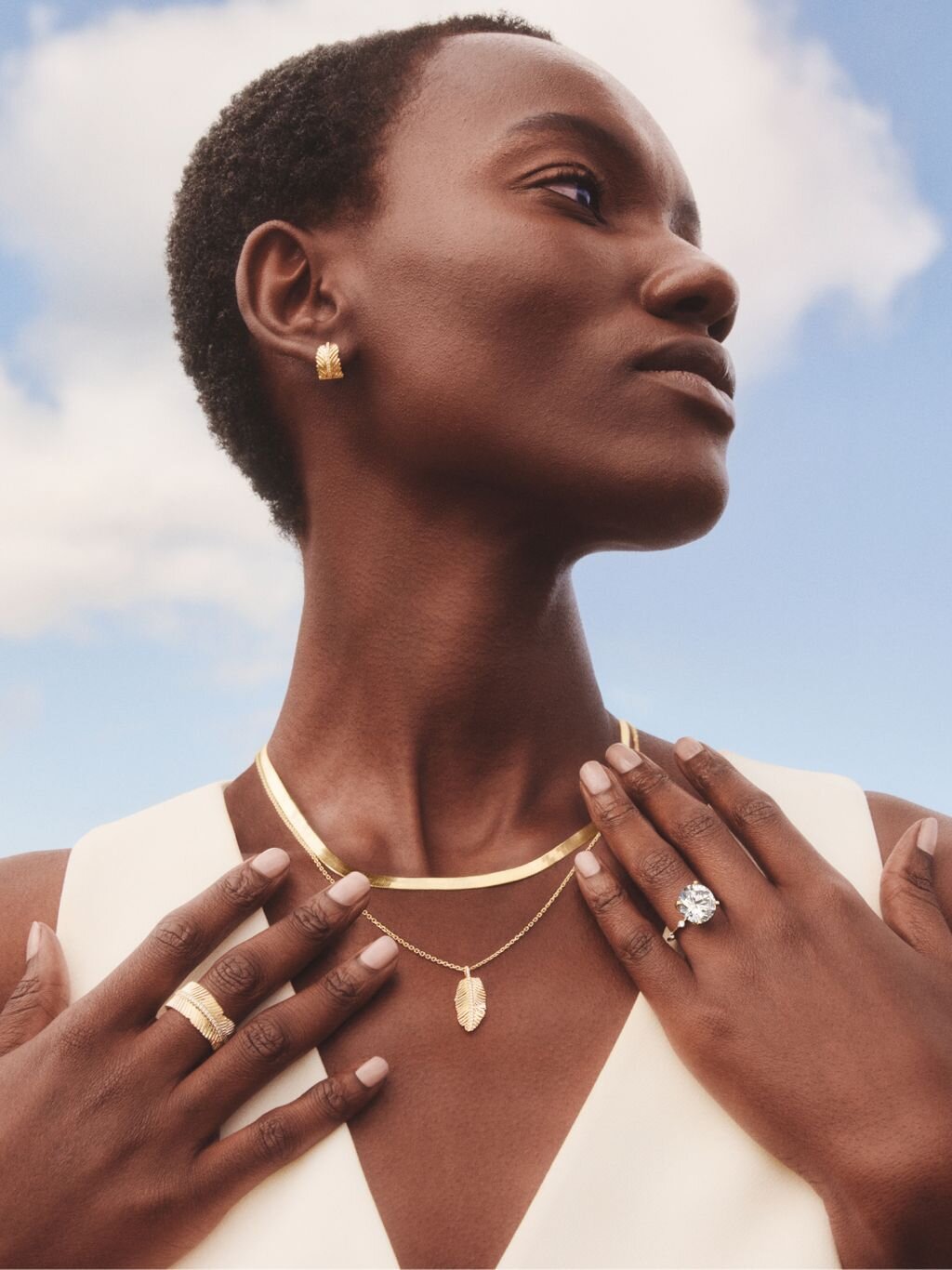 Person wearing multiple delicate diamond necklaces and jewelry pieces against a natural outdoor background