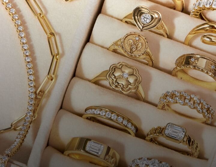 Close-up of multiple gold rings and jewelry bracelets arranged on light surface