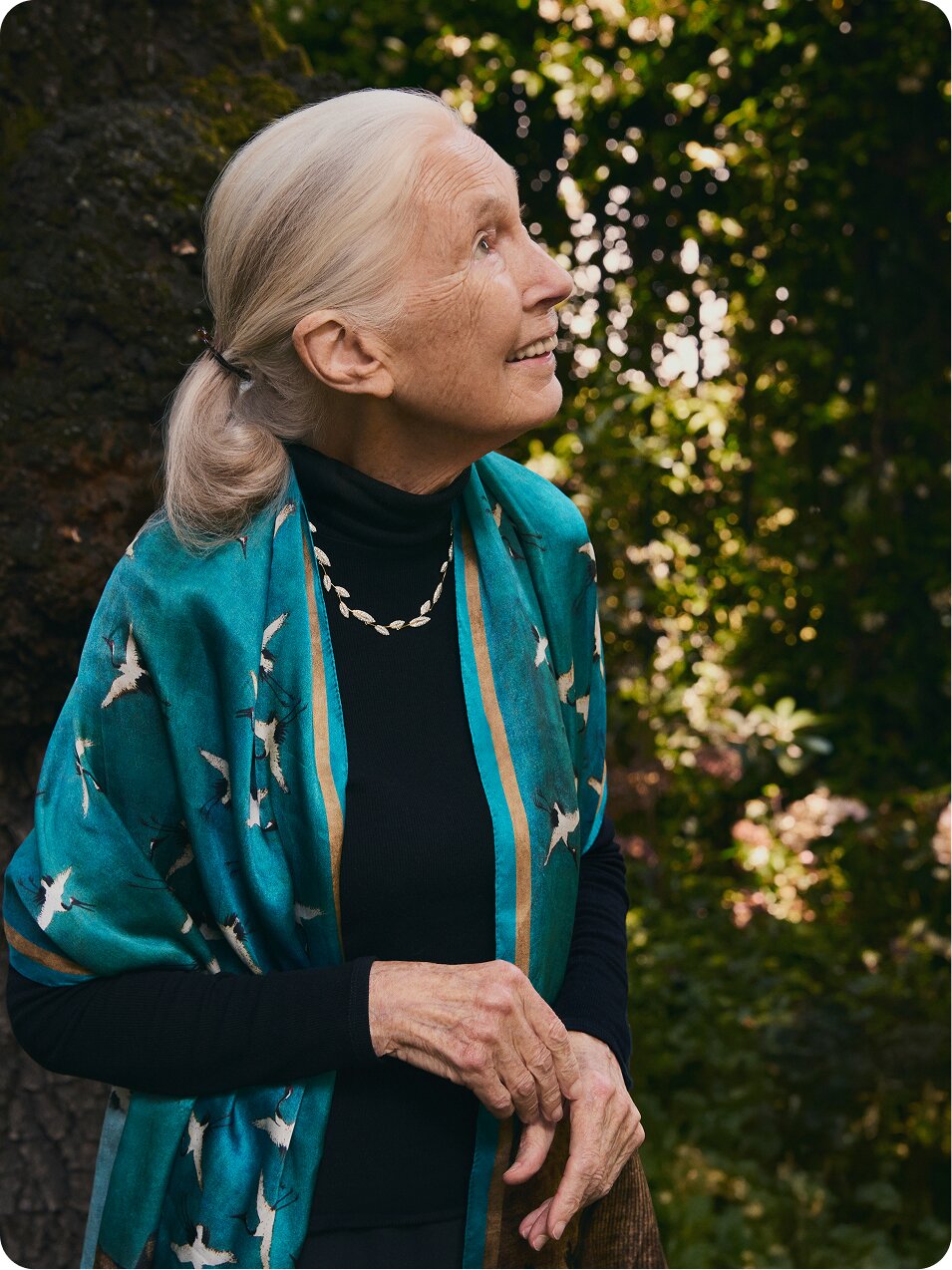 Dr. Jane Goodall smiling while wearing dark clothing and a leaf pendant necklace
