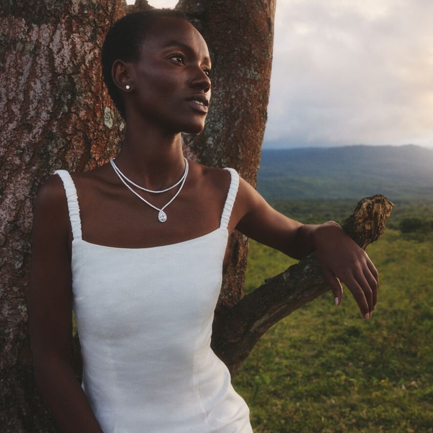 Woman in a white dress wearing jewelry outdoors against a natural background