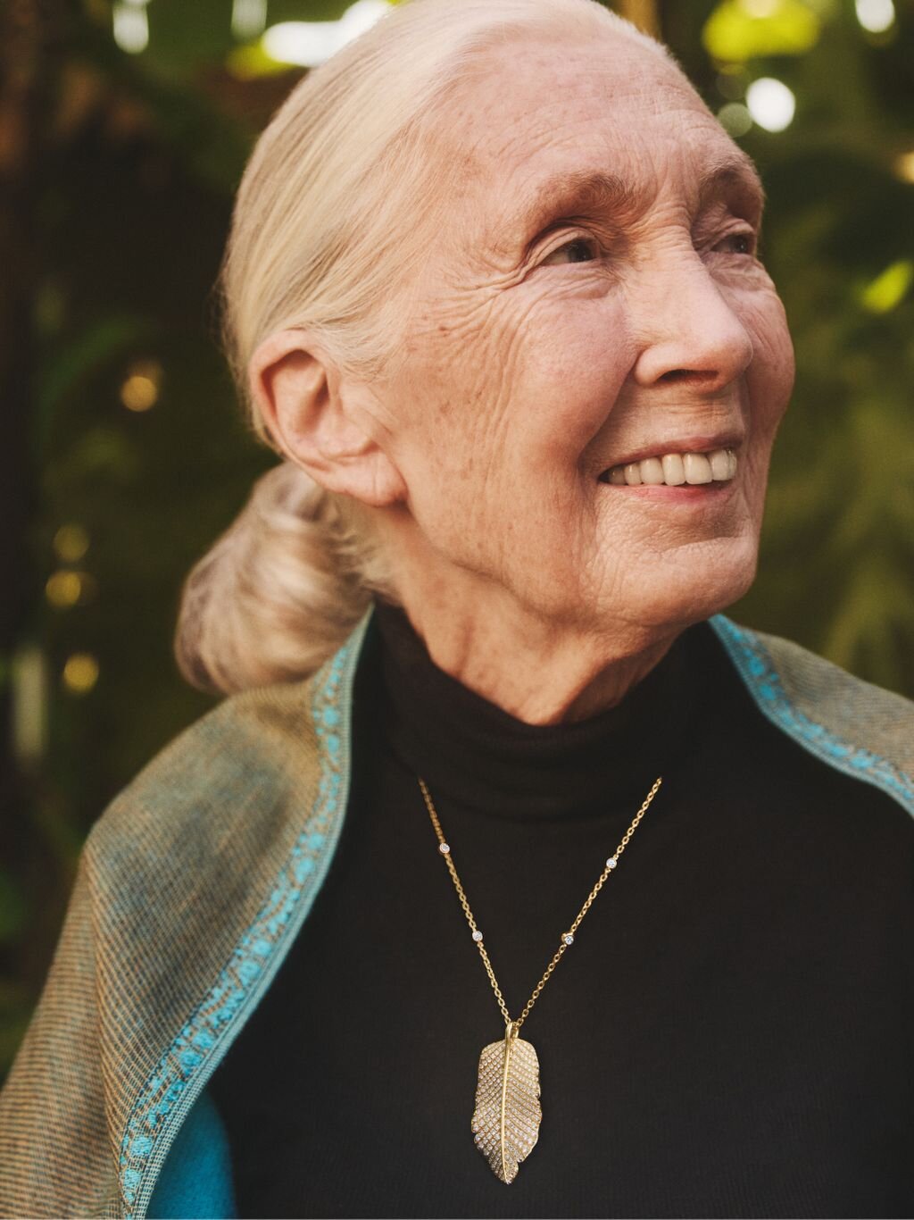 Dr. Jane Goodall smiling while wearing dark clothing and a leaf pendant necklace