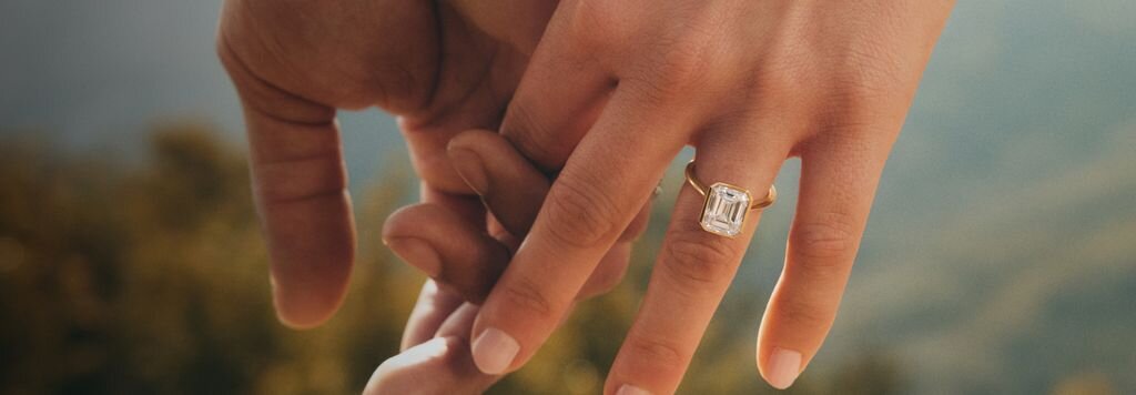 Close-up of hands displaying an emerald-cut diamond ring against natural background