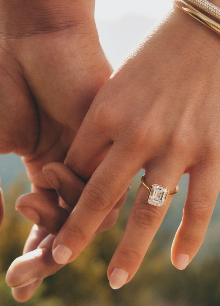 Close-up of hands displaying an emerald-cut diamond ring against natural background