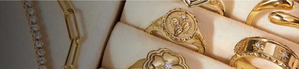 Close-up of multiple gold rings and jewelry bracelets arranged on light surface