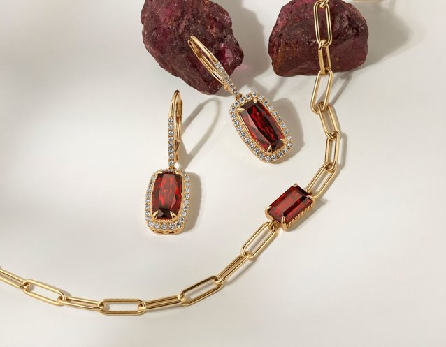 A garnet bracelet with matching earrings next to raw garnet stone