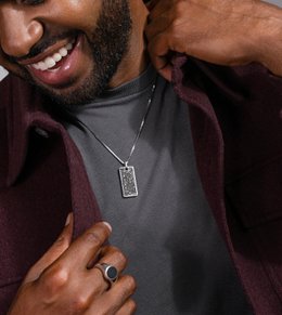 A man wearing a fashion ring and a dog tag pendant