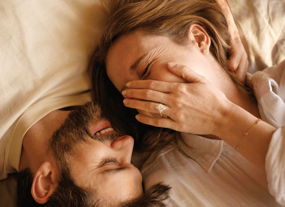 A couple laughing together laying on a bed