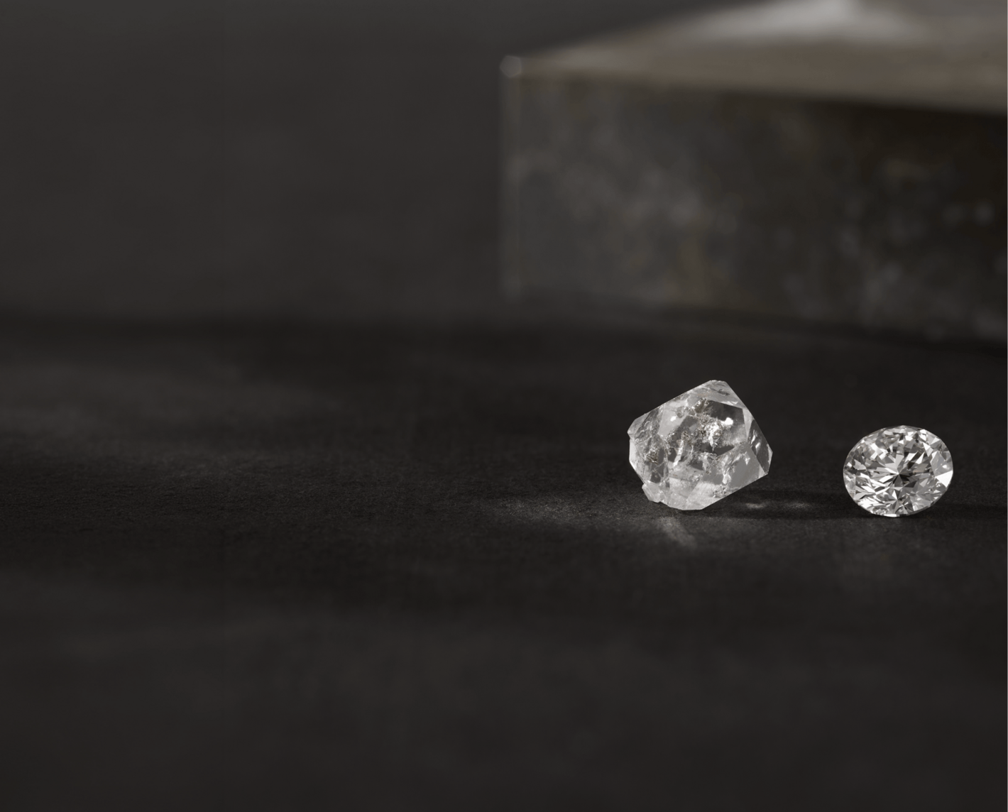 A rough cut diamond and a fully finished natural diamond on a dark background