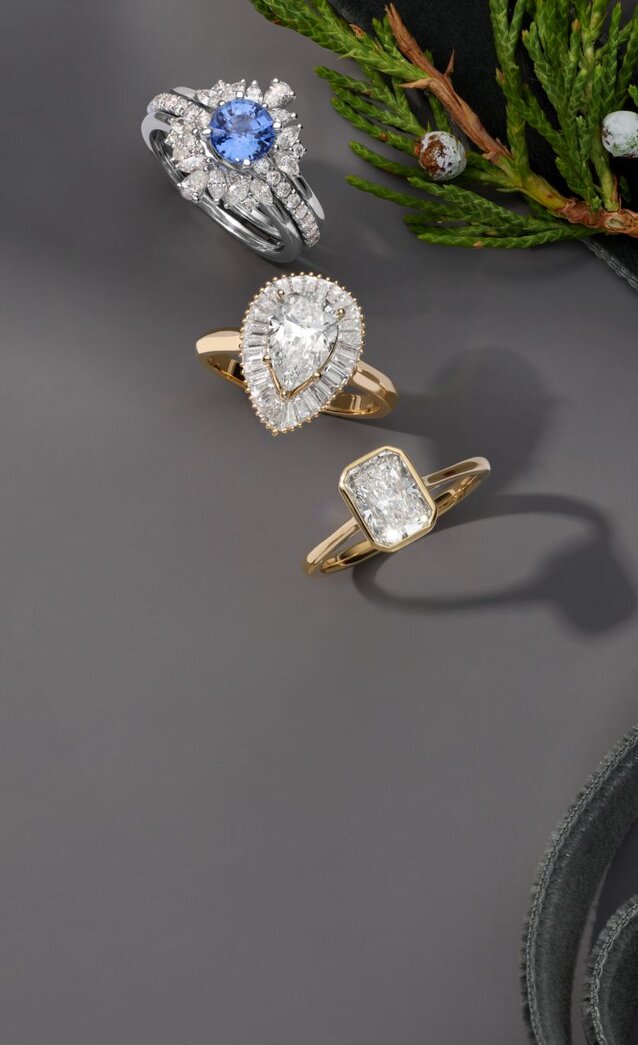 Three engagement rings next to an evergreen branch and a holiday ribbon