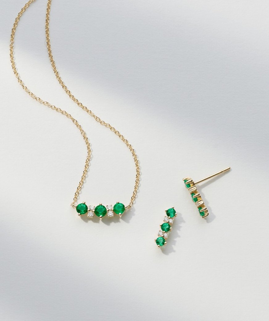 Image: A dazzling jewelry set featuring an emerald and diamond yellow gold necklace and a pair of matching earrings. The necklace showcases a stunning emerald gemstone paired with brilliant diamonds, on a yellow gold chain. The earrings mirror the necklace's design, creating a coordinated and luxurious jewelry ensemble.