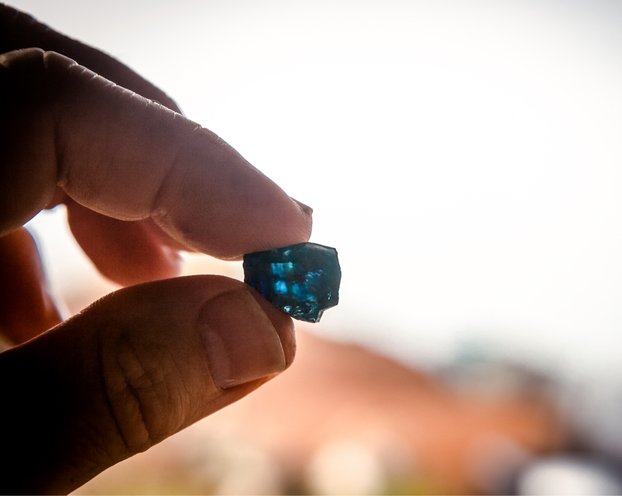 A hand holding a rough sapphire