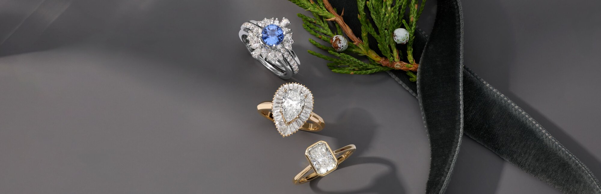 Three engagement rings next to an evergreen branch and a holiday ribbon