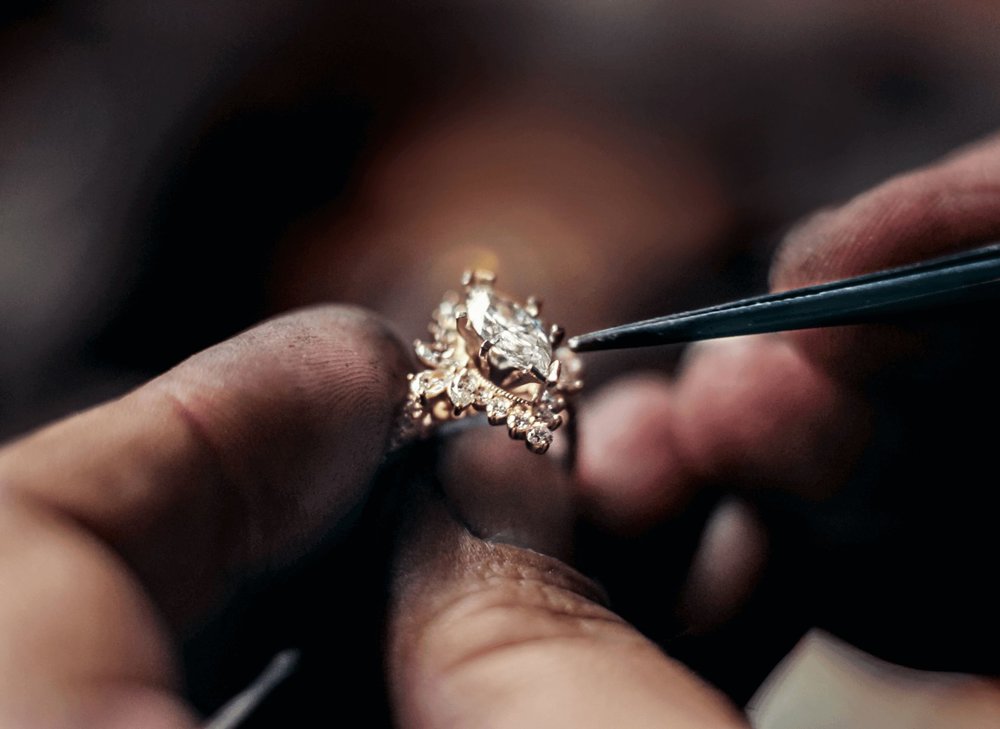 A jeweler's hands holding a diamond halo engagement ring