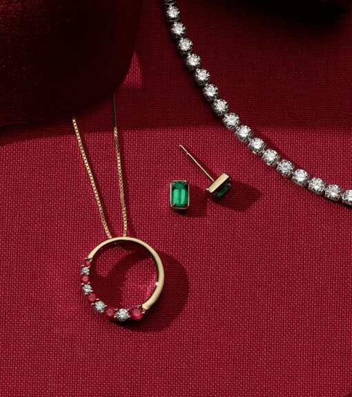 A diamond tennis bracelets next to a pair of gemstone solitaire earrings and a gemstone and diamond fashion pendant.