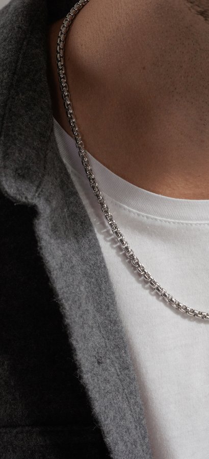 Closeup of a person wearing a white gold chain necklace with white t-shirt under a gray collared shirt.