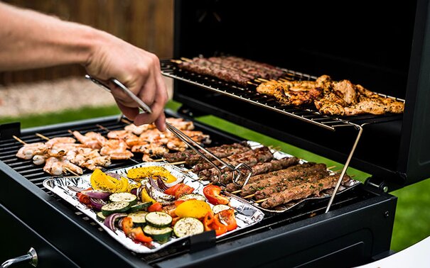 A person using tongs to cook on an outdoor grill.
