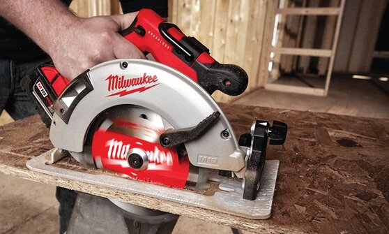 A cordless Milwaukee saw cutting a peice of plywood.