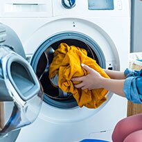 A yellow shirt being added to a front load washing machine.