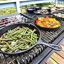 Cast iron cookware cooking vegetables on a grill.