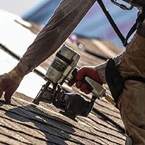A roofer uses a nail gun on a roof.