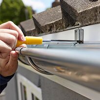 A hand tightens hardware holding up a roof gutter.