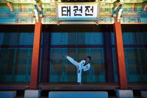 A martial artist intensely performing a move while other students watch in the background.
