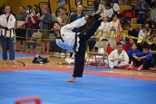 A martial artist intensely performing a move while other students watch in the background.