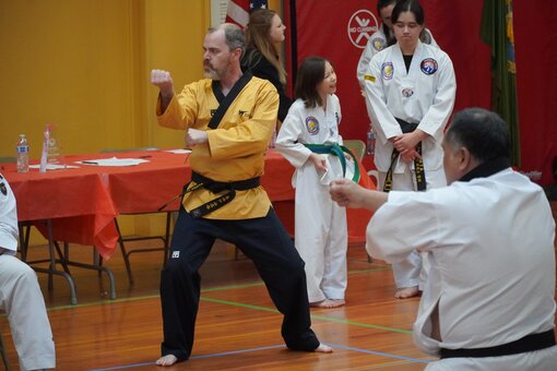 A martial artist intensely performing a move while other students watch in the background.