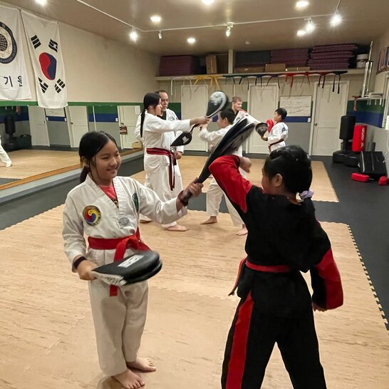 Two lines of students partnered together with one line using foam pads to help the other line practice blocking above their heads.