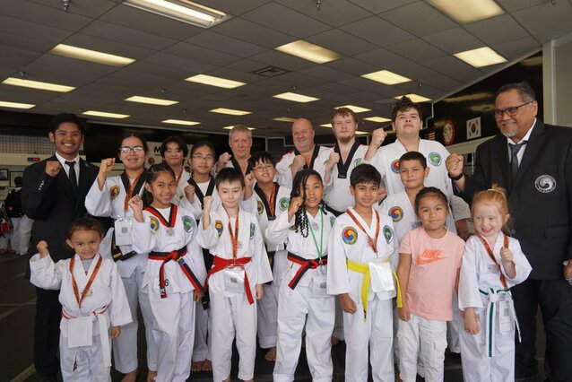 A group of people in martial arts uniforms celebrating as a group with their fists held high.