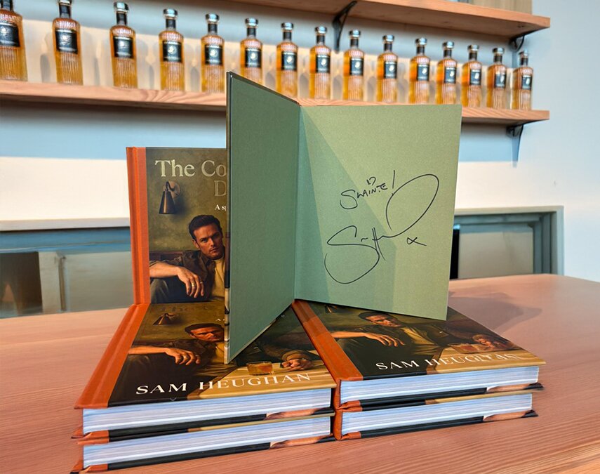 A stack of The Cocktail Diaries: A Spirited Adventure books signed by Sam Heughan.