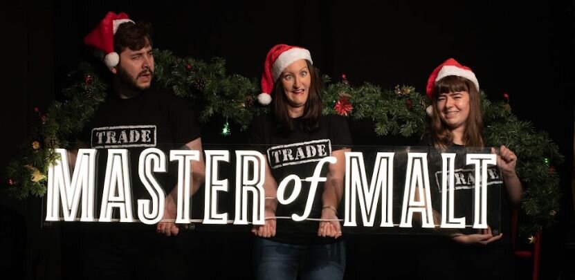 Master of Malt Trade team with Santa hats holding a MoM logo light