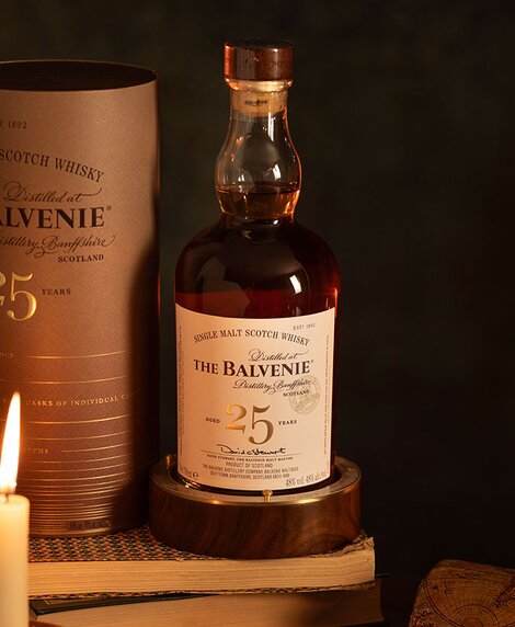 A bottle of Balvenie 25 Year Old Rare Marriages whisky on top of a stack of books next to a candle. 