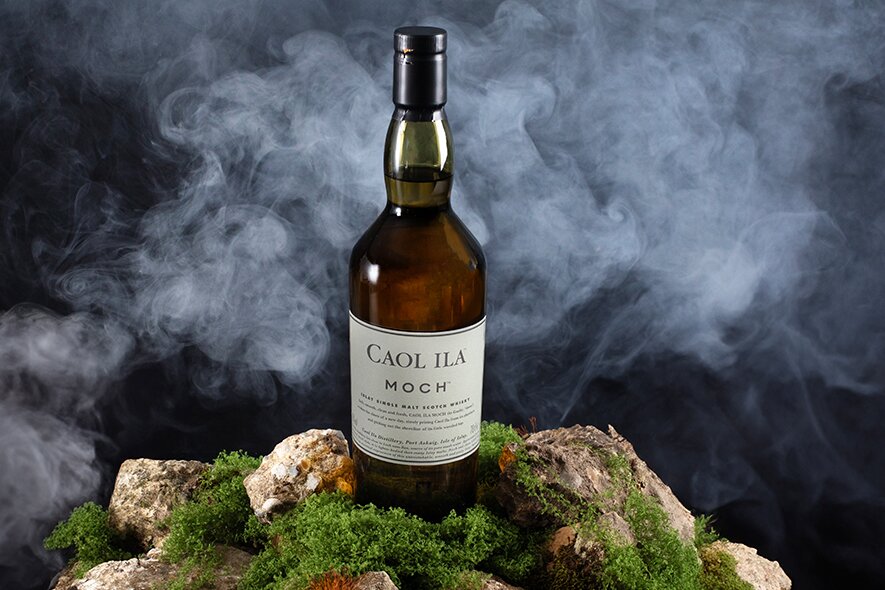 Caol Ila Moch whisky on a mossy rock surface surrounded by fog.