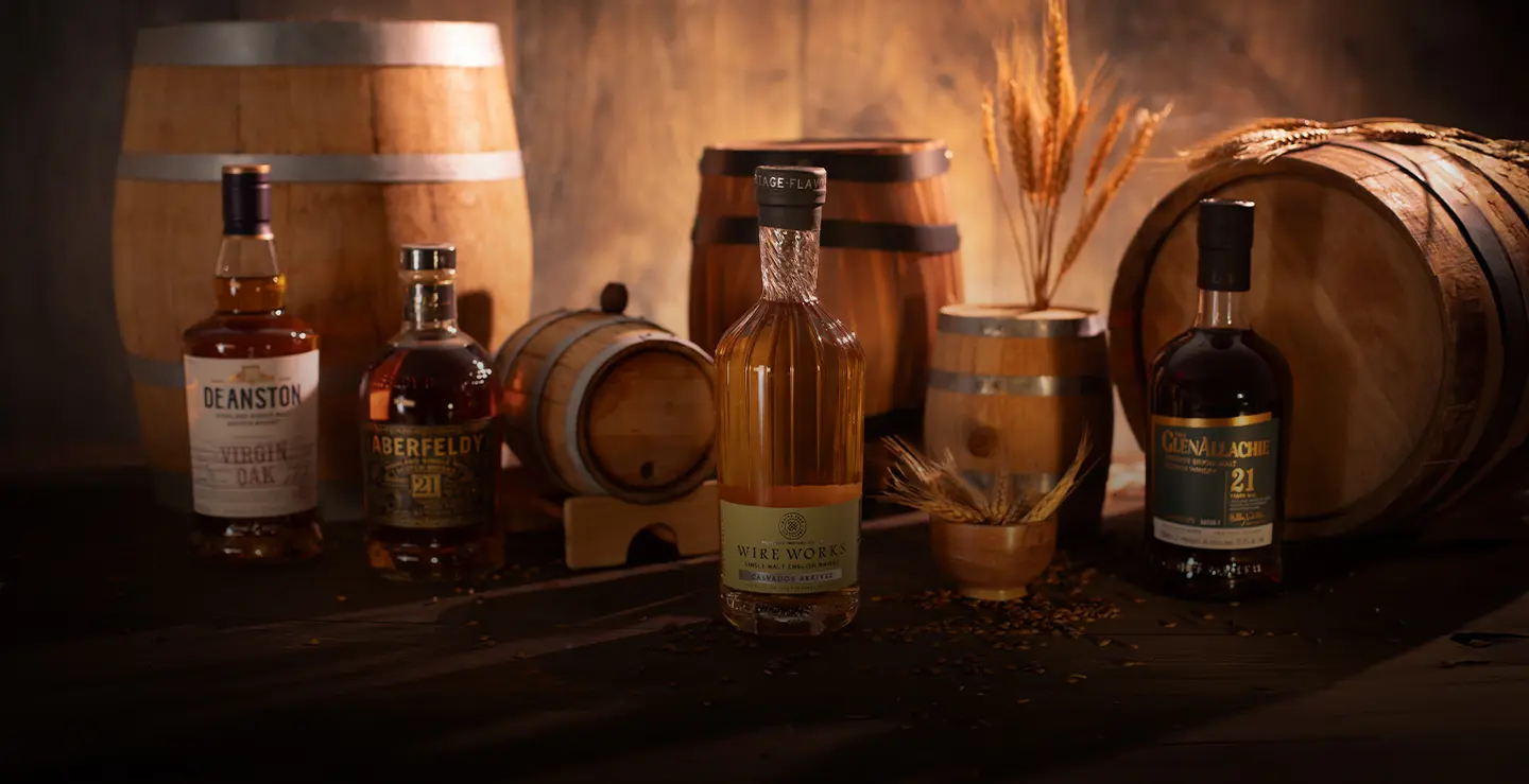 Four bottles of cask influenced whisky surrounded by barrels and barley.