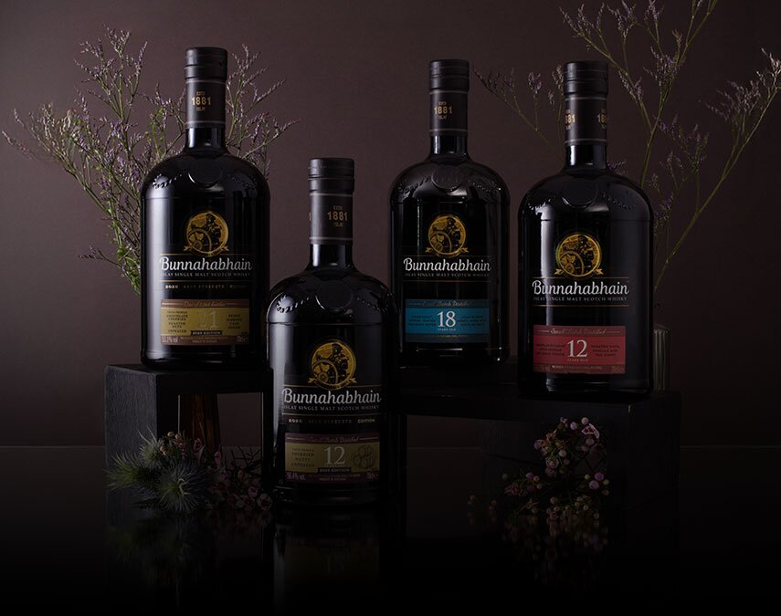 Four bottles of Bunnahabhain whisky surrounded by thistles on a brown background.
