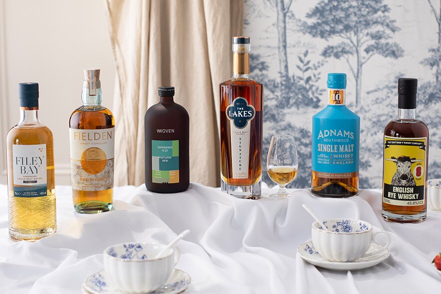 Six bottles of English whisky against blue floral wallpaper.