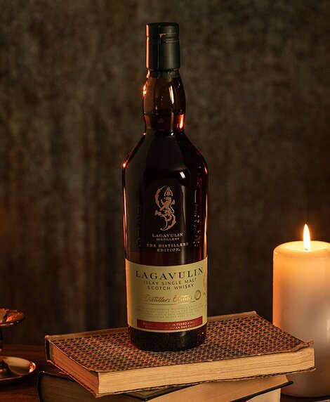 A bottle of Lagavulin Distillers Edition whisky on top of a stack of books next to a candle. 