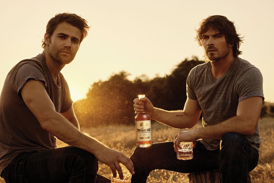 Paul Wesley and Ian Somerhalder holding bottles of Brother's Bond whiskey.