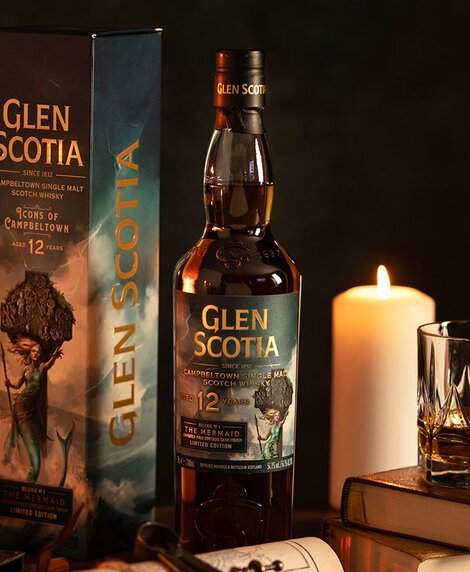 A bottle of Glen Scotia 12 year old - The Mermaid whisky next to a stack of books and a candle. 