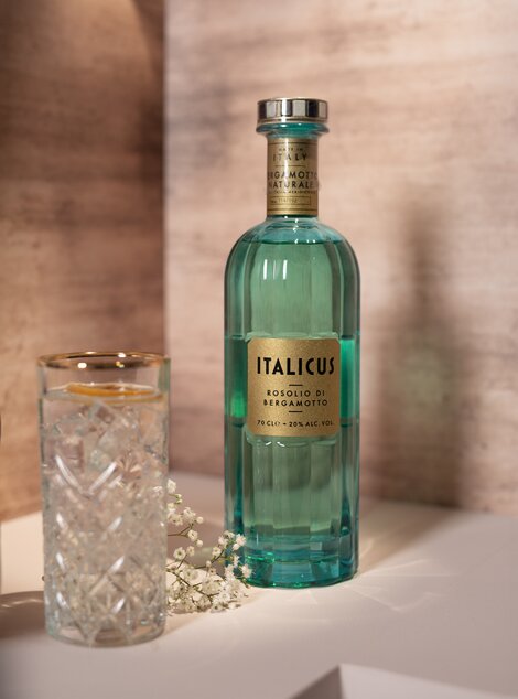 A bottle of Italicus liqueur against a pink and beige background. 