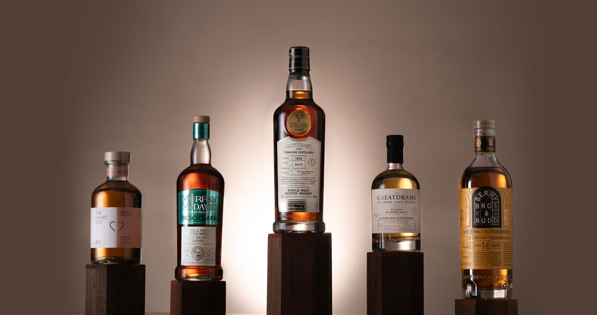 Five bottles of whisky on dark wood plinths against a beige background.